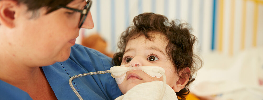 Bild: Die Atmungstherapeutin der Kinderklinik hält ein beatmetes Kind im Arm